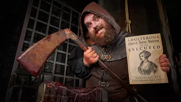 The Rotten Royals executioner is posing inside the London Dungeon with his axe and sign detailing the execution of Anne Boleyn. The London Dungeon is a popular tourist attraction in London that offers a variety of interactive experiences based on London's history.